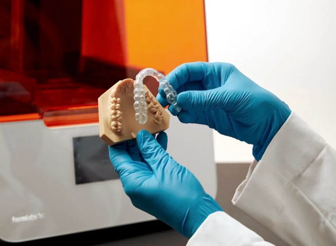 A technician holding a finished aligner and its model beside the printer